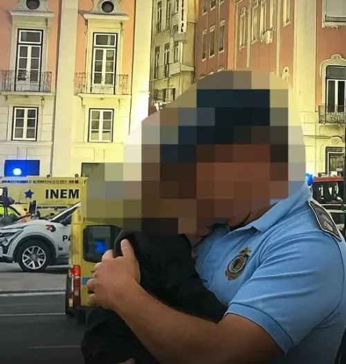 Um policial abraça uma criança após a tragédia de Lisboa que teve um forte impacto psicológico em todos. A cena capturada no meio de uma estrada é pixada para proteger a privacidade da criança.
